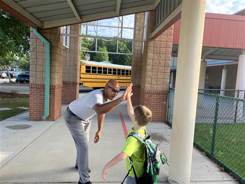 Assistant superintendent Eric Terrell high fiving a student outside a school